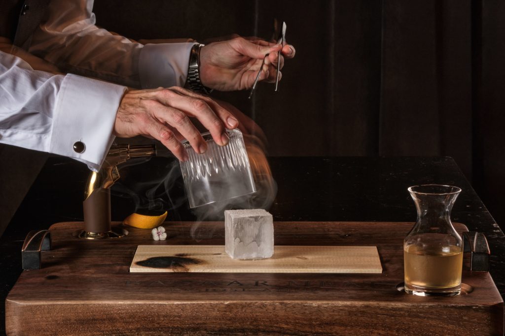 Bartender hands creating the smoked Manhattan cocktail.