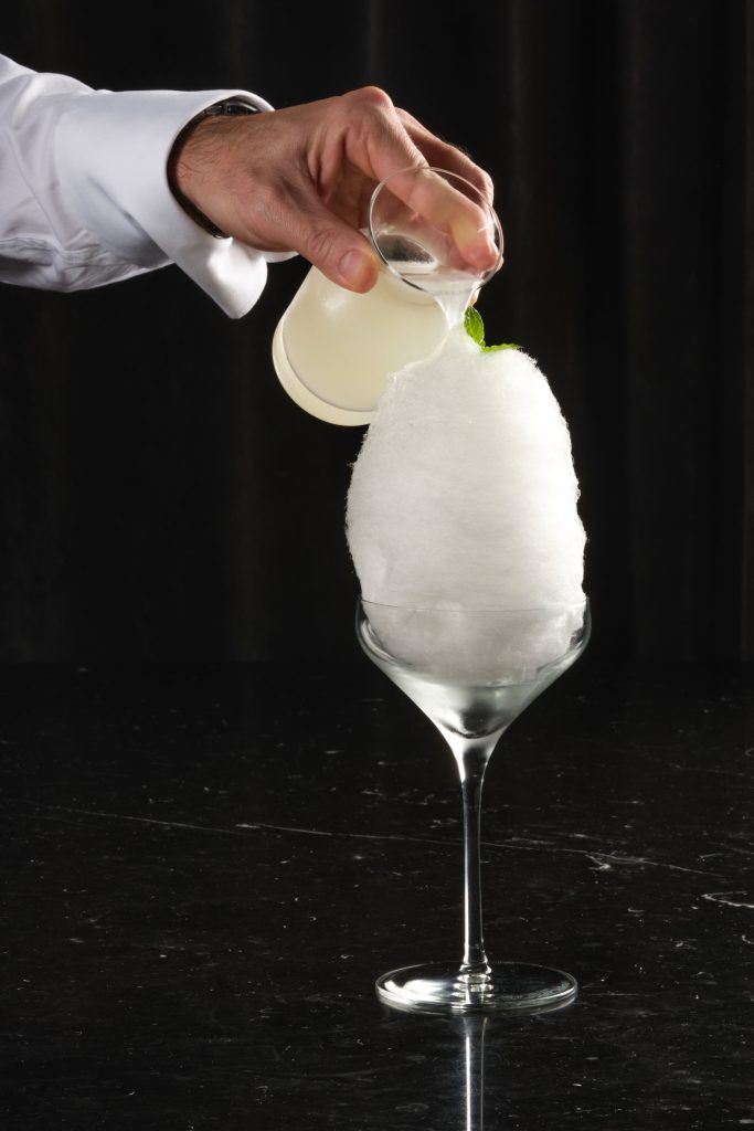 Bartender hands creating the Magic Mojito cocktail, featuring cotton candy pour over.