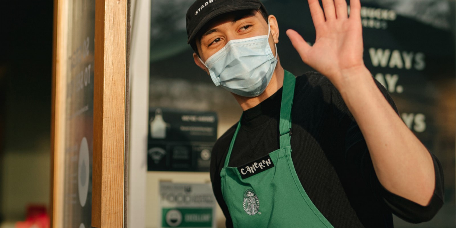 Starbucks barista with a mask opening door and waving