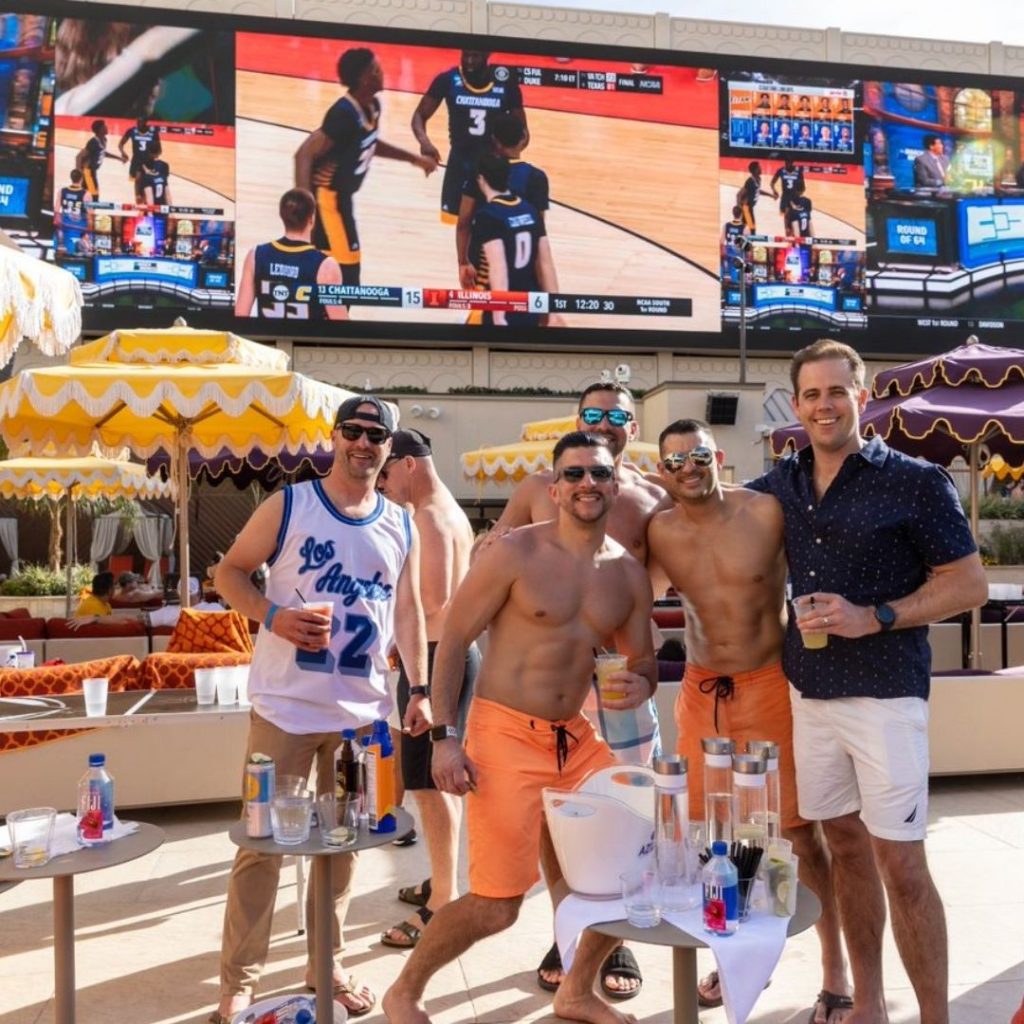 Group of guys hanging out at AZILO Ultra Pool with drinks. The guys are watching sports on the huge screen overlooking the venue.