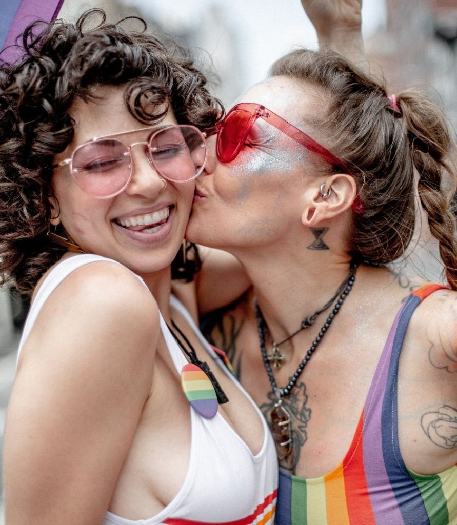 Two girls kissing at Pride wearing rainbow clothes
