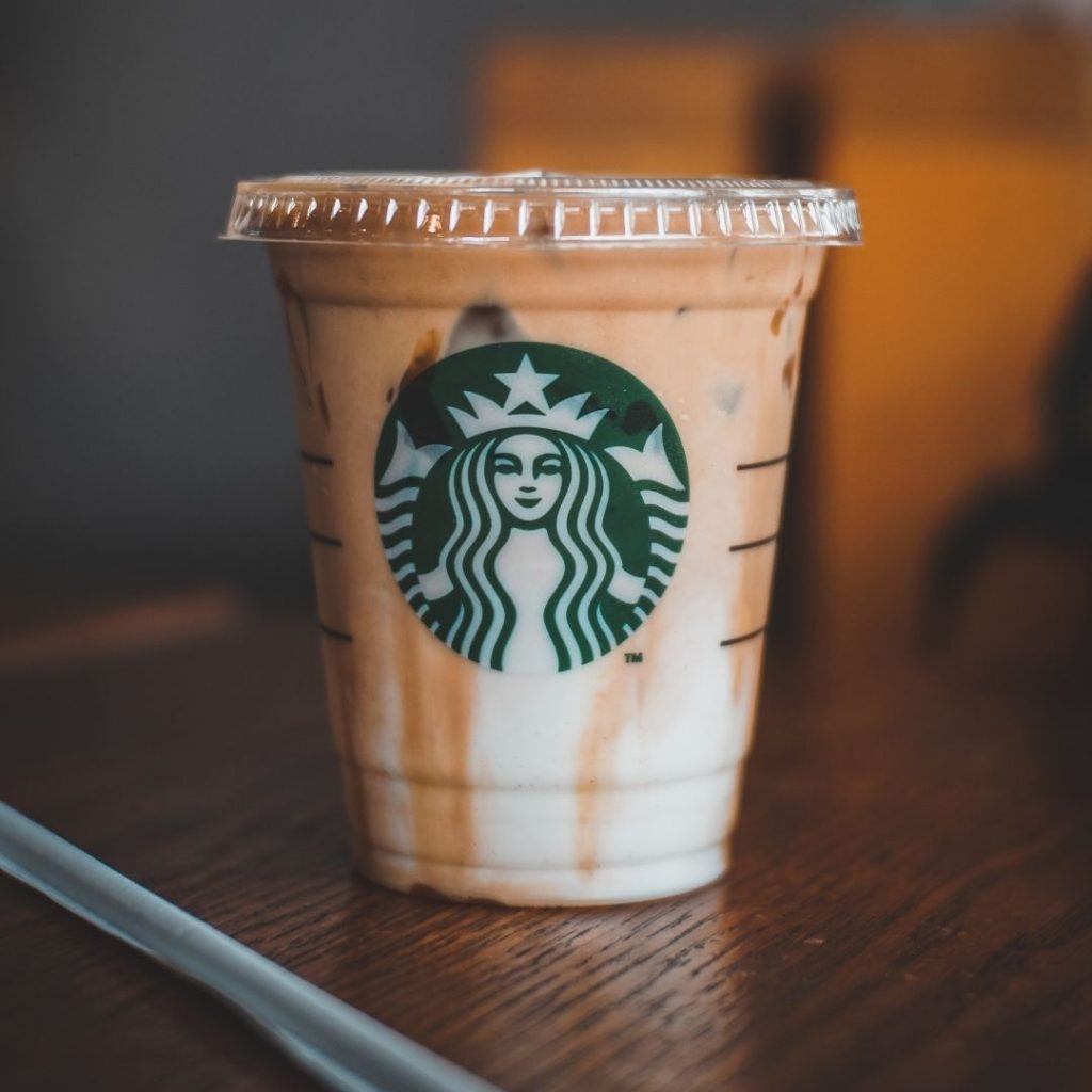A iced caramel machiatto witting on a wooden table with a straw sitting on the table next to it