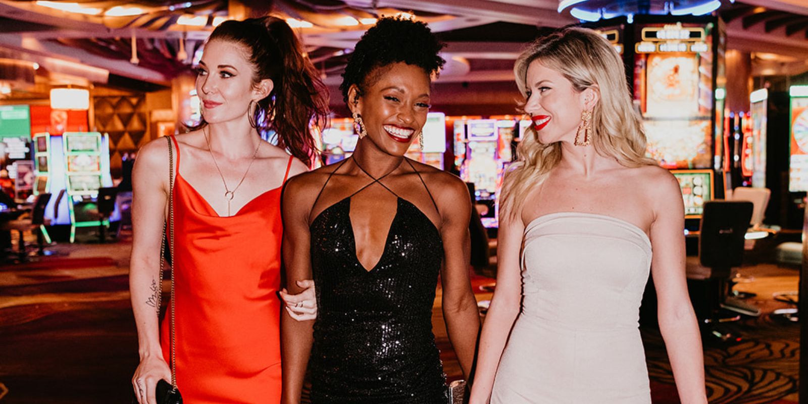 3 women walking arm in arm on the casino floor laughing and smiling