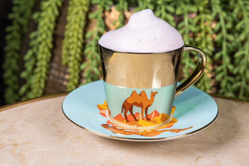 Camel themed cup at The Tangier showing foam inside and a plant behind the drink